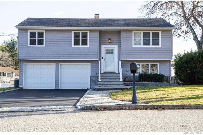 Raised ranch featuring an attached garage, asphalt driveway, a chimney, and a front lawn