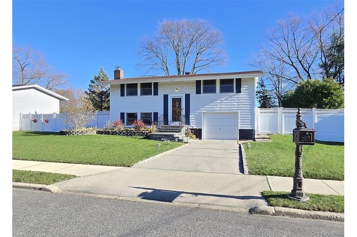 Raised ranch with a chimney, concrete driveway, and an attached garage