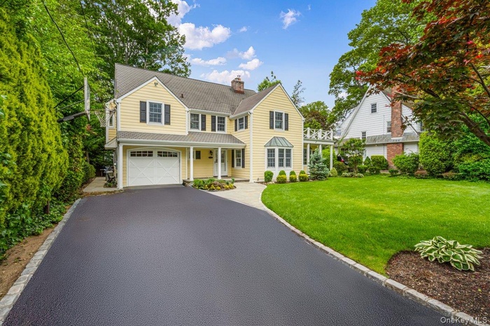 View of front of home with covered porch, a front yard, asphalt driveway, a garage, and a chimney