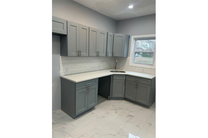 Kitchen featuring gray cabinets, light stone counters, and light marble finish floors