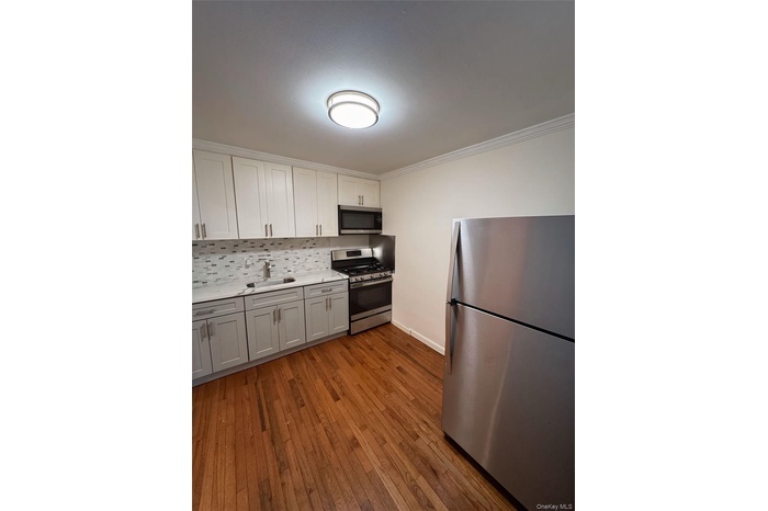 Kitchen featuring appliances with stainless steel finishes, dark wood-type flooring, decorative backsplash, white cabinetry, and gray cabinets