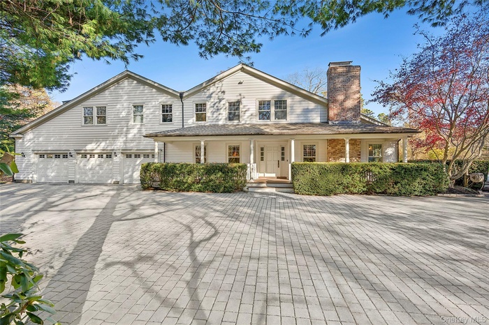 View of front of house with a chimney, decorative driveway, covered porch, and an attached garage