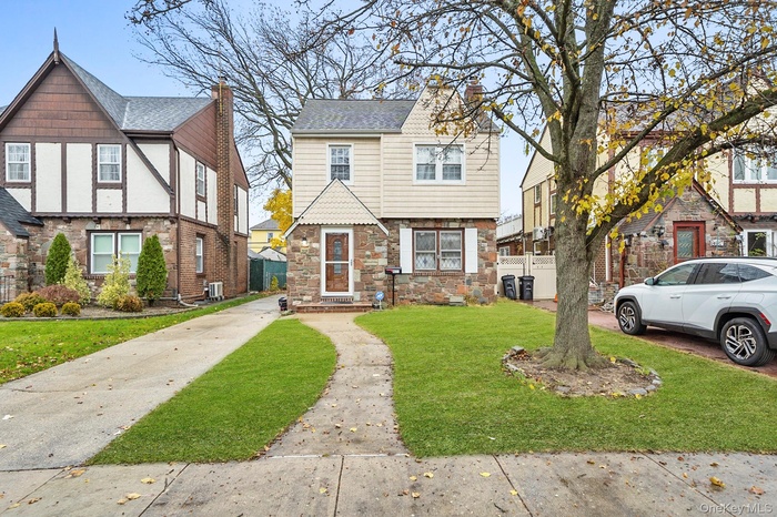 English style home with stone siding, a front lawn, and concrete driveway