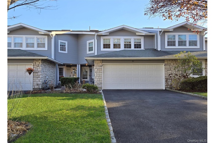Traditional home featuring stone siding, asphalt driveway, a front lawn, and a shingled roof