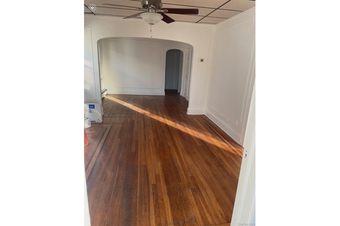 Empty room with arched walkways, dark wood finished floors, ceiling fan, and a baseboard radiator