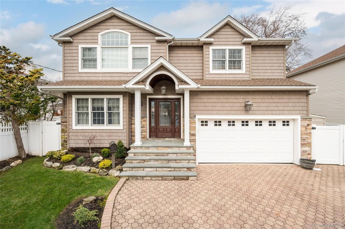 View of front facade featuring decorative driveway, a garage, a shingled roof, and stone siding