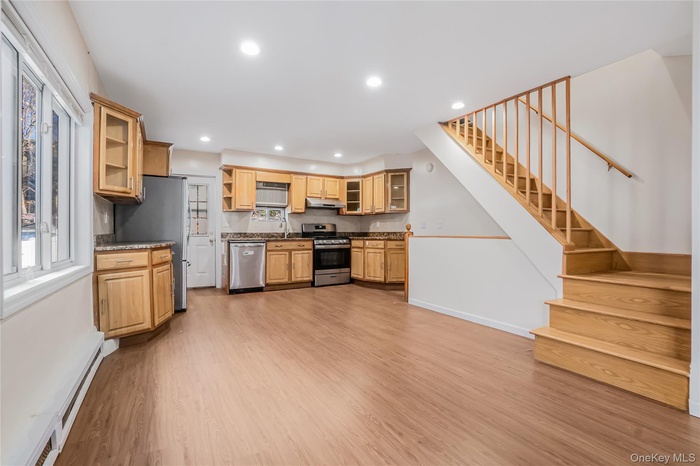 Kitchen with glass insert cabinets, plenty of natural light, appliances with stainless steel finishes, a baseboard radiator, and recessed lighting