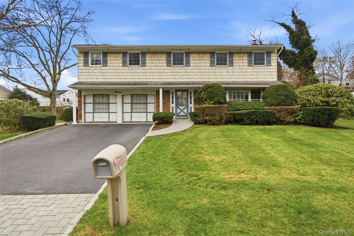 View of front of home with driveway, a front lawn, an attached garage, a chimney, and brick siding