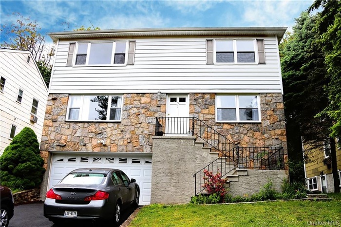 Colonial house featuring stone siding, a garage, driveway, and a front yard