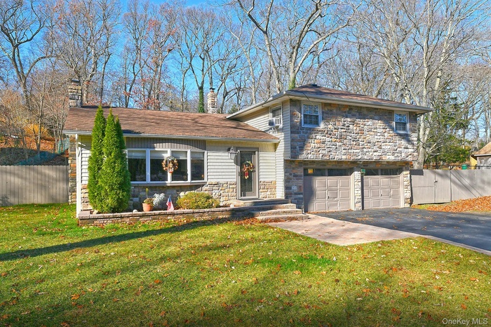 Tri-level home featuring a chimney, asphalt driveway, a garage, and stone siding