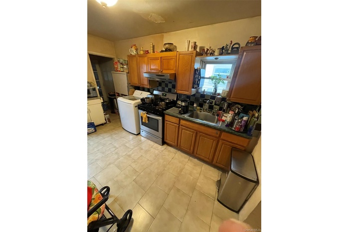 Kitchen with brown cabinets, stainless steel range with gas cooktop, washer / clothes dryer, under cabinet range hood, and dark stone countertops