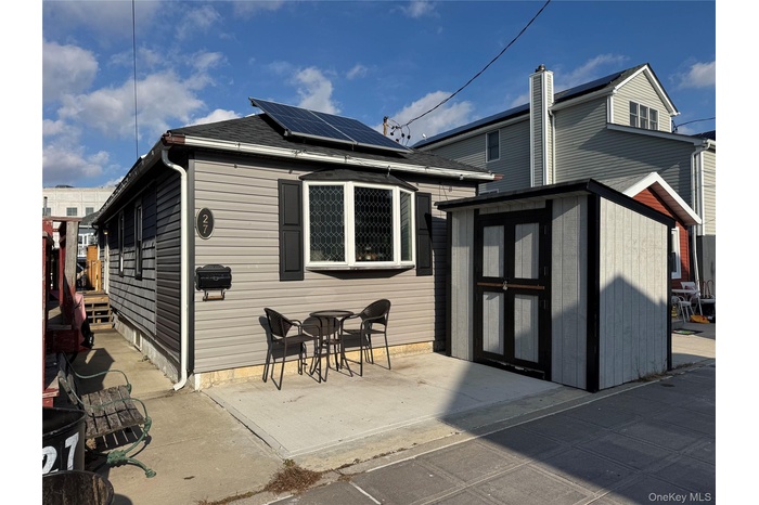 Back of house with roof mounted solar panels, a storage unit, a patio area, and roof with shingles