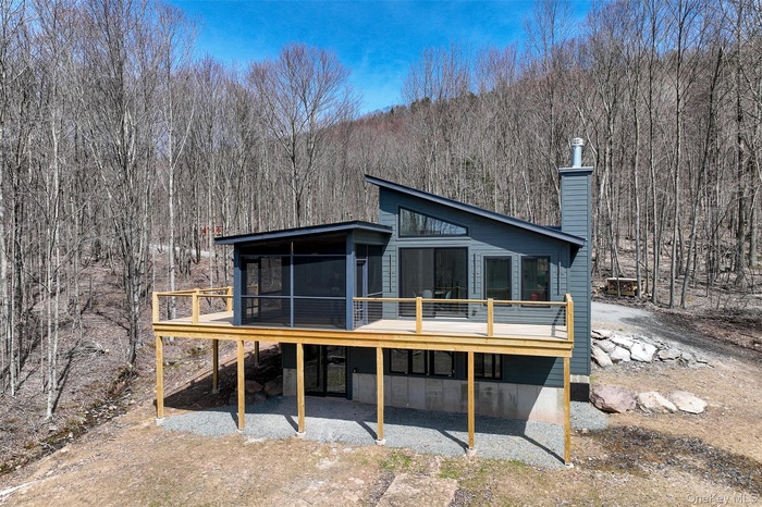 Back of property with a sunroom, a deck, a forest view, and a chimney
