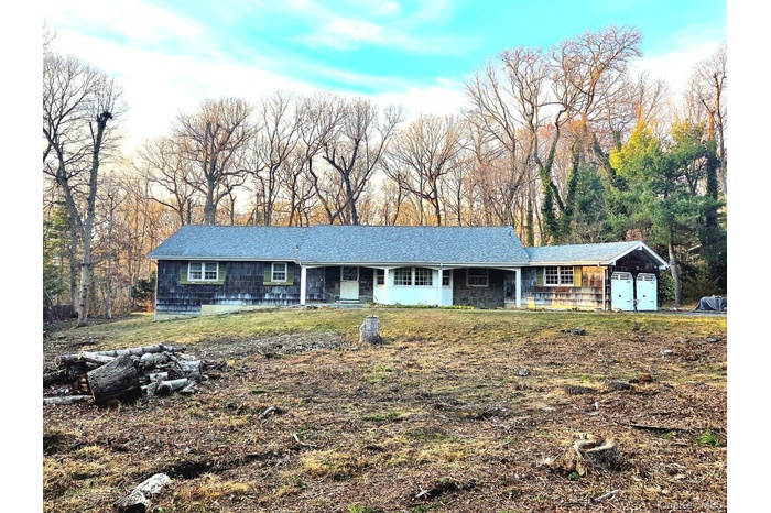 Single story home with a front yard, covered porch, a garage, and view of scattered trees