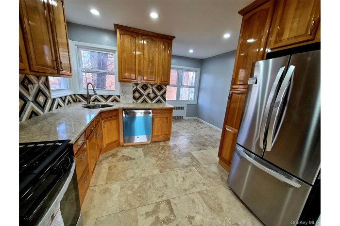 Kitchen featuring stainless steel appliances, brown cabinets, light stone counters, recessed lighting, and tasteful backsplash