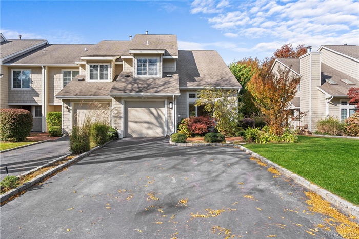 Shingle-style home featuring a front lawn, a garage, driveway, roof with shingles, and a residential view