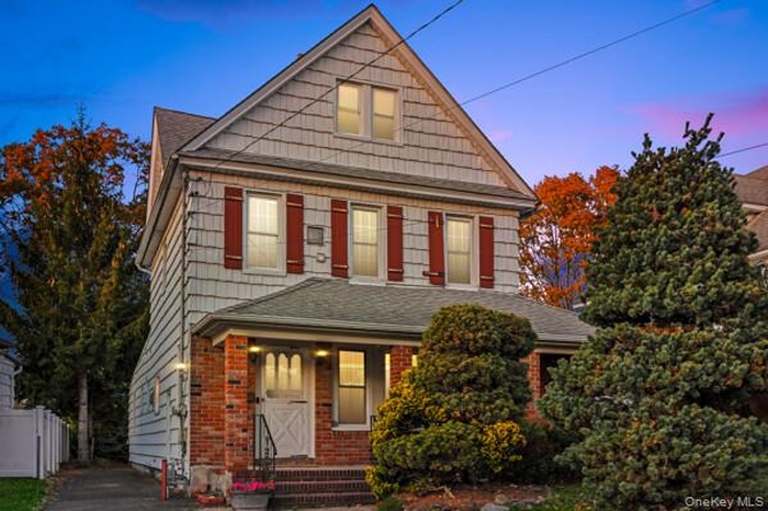 Front of home with a shingled roof, covered porch, and brick/vinyl siding