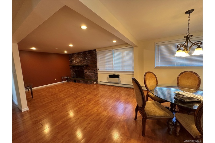 Dining space with wood finished floors, an AC wall unit, a fireplace, recessed lighting, and baseboard heating