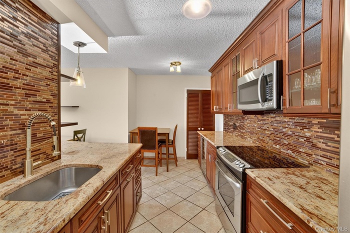 Kitchen featuring tasteful backsplash, appliances with stainless steel finishes, hanging light fixtures, brown cabinetry, and a textured ceiling
