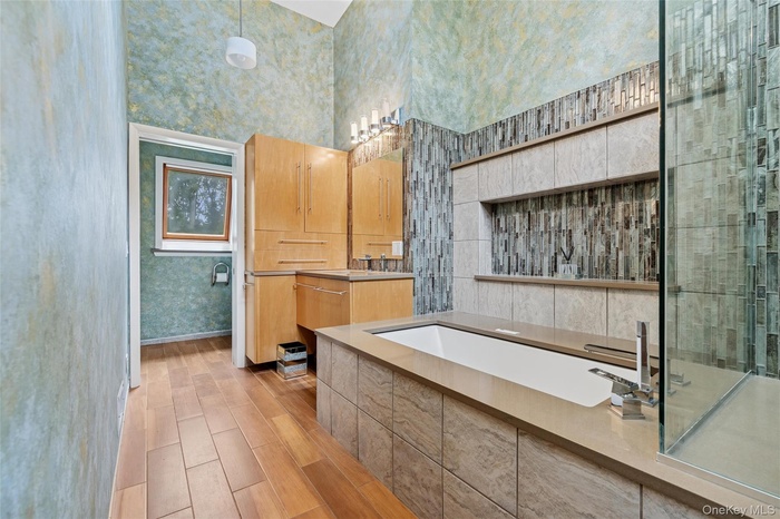 Full bath vanity, a garden tub, wood tiled floors, and a towering ceiling