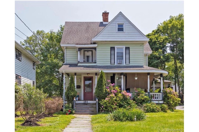 View of front of property featuring covered porch, a shingled roof, a chimney, and a front yard