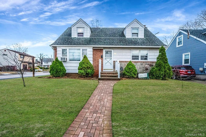 Cape cod-style house featuring a shingled roof, brick siding, and a front lawn