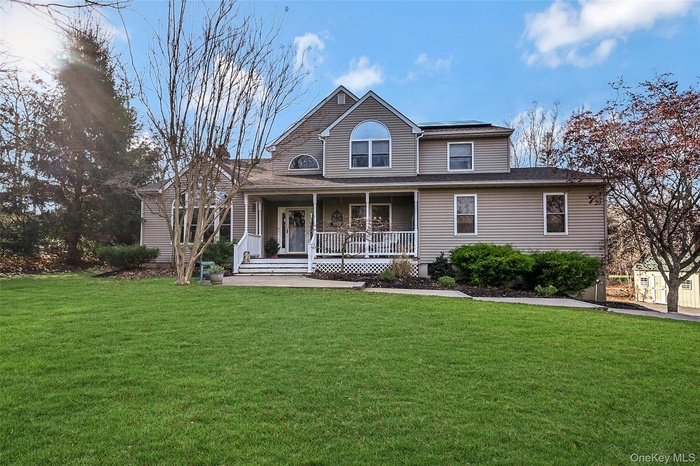 View of front of house featuring covered porch, a front lawn, and roof with shingles