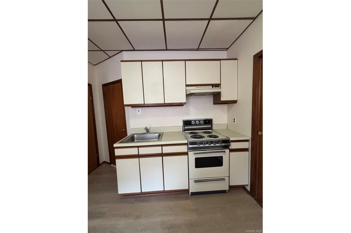 Kitchen with white range with electric cooktop, white cabinetry, light countertops, under cabinet range hood, and light wood-style flooring