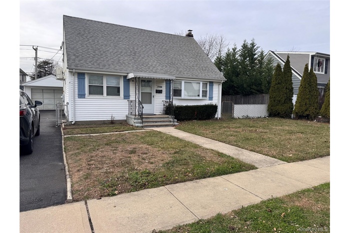 View of front of house with a shingled roof, a garage, a chimney, and an outbuilding