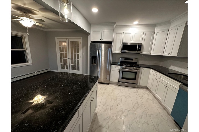 Kitchen featuring light marble finish flooring, stainless steel appliances, white cabinets, a baseboard radiator, and dark stone countertops