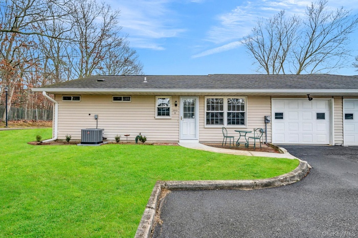 Rear view of house featuring driveway, an attached garage, a yard, and a shingled roof