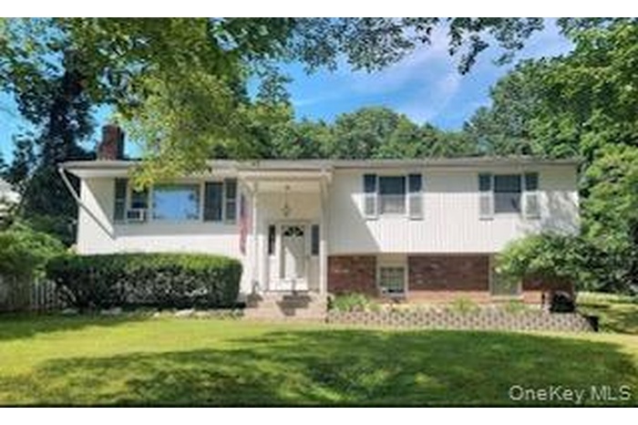 Raised ranch featuring a front yard, a chimney, and brick siding