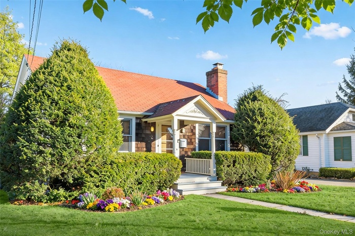 View of front of house with a front lawn, a chimney, and roof with shingles