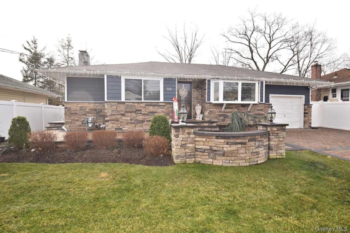 Ranch-style house featuring a chimney, a patio area, decorative driveway, and stone siding