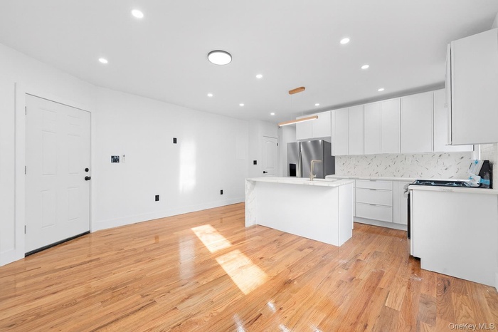 Kitchen featuring a kitchen island with sink, recessed lighting, white cabinetry, gas stove, and stainless steel fridge with ice dispenser