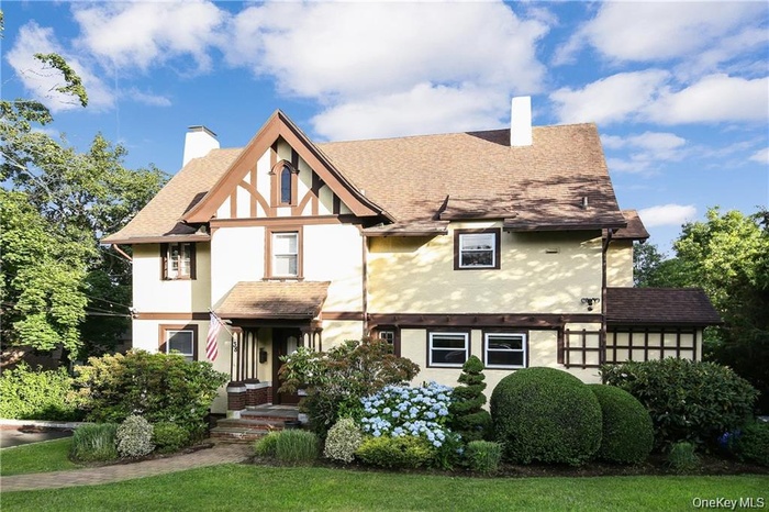 Tudor house with a chimney, stucco siding, and roof with shingles
