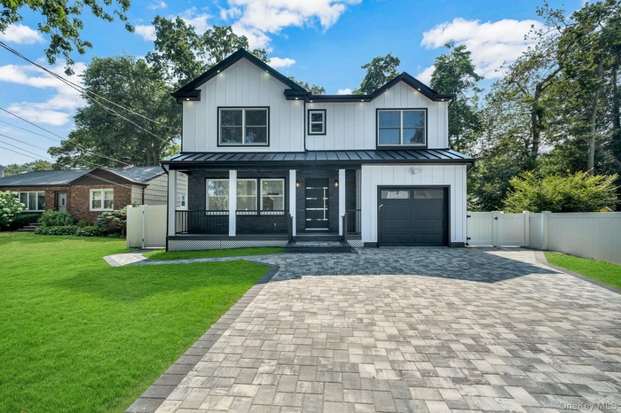 Modern inspired farmhouse with a standing seam roof, a gate, covered porch, and decorative driveway