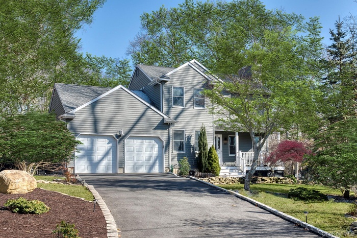 Traditional home with asphalt driveway, an attached garage, a porch, and roof with shingles