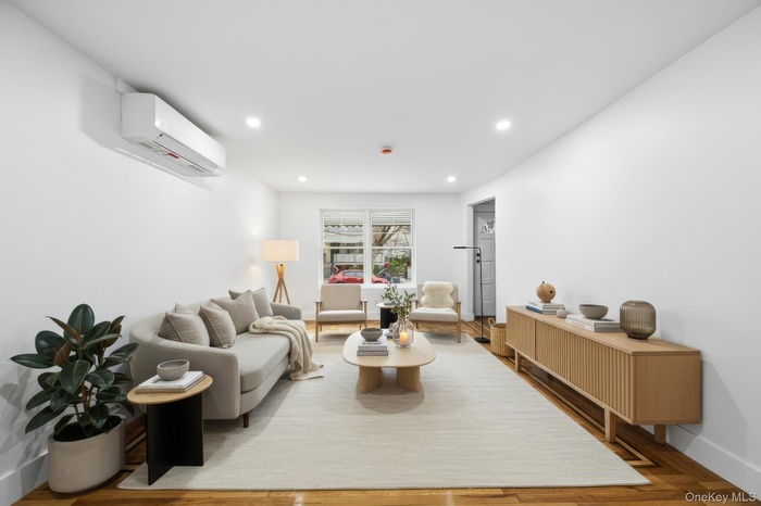 Living room with a wall mounted air conditioner, recessed lighting, and wood finished floors