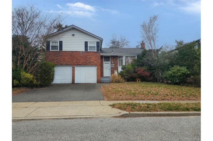 Tri-level home with asphalt driveway, brick siding, an attached garage, and a chimney