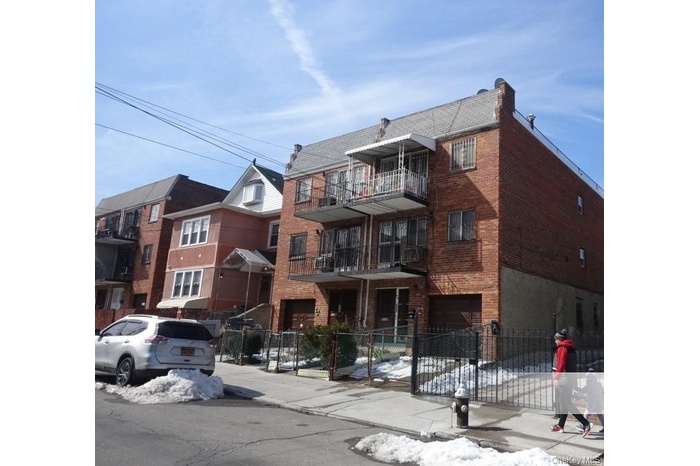 Snow covered property featuring a fenced front yard, an attached garage, and a view of apartment building / complex