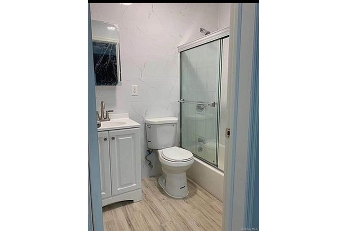 Bathroom with vanity, light wood-style floors, and combined bath / shower with glass door
