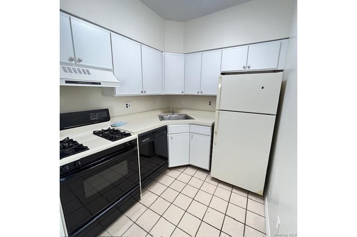 Kitchen with black appliances, light countertops, white cabinets, under cabinet range hood, and light tile patterned flooring