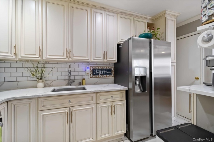 Kitchen featuring cream cabinetry, stainless steel fridge, light stone countertops, and ornamental molding