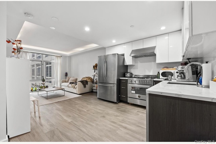 Kitchen with white cabinets, appliances with stainless steel finishes, modern cabinets, light stone counters, and light wood-style flooring