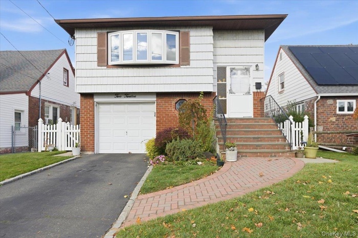 View of front facade with brick siding, driveway, and a garage