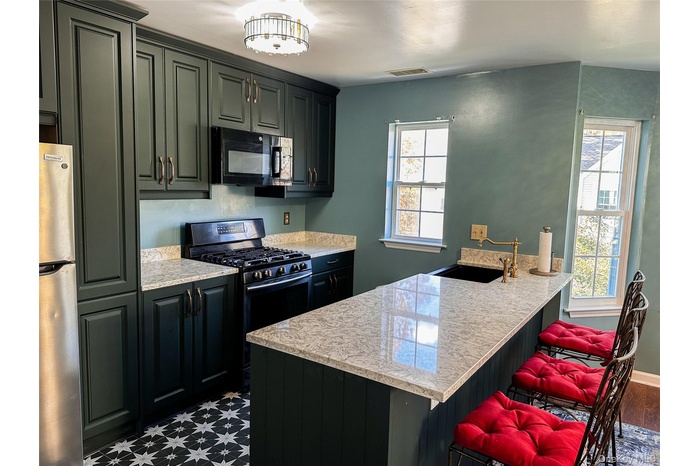 Kitchen featuring gas stove, a breakfast bar area, black microwave, freestanding refrigerator, and a peninsula