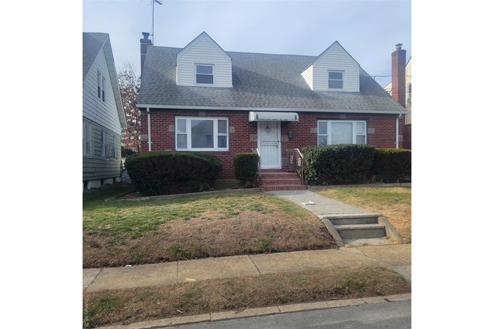 Cape cod-style house with brick siding, a front yard, and roof with shingles