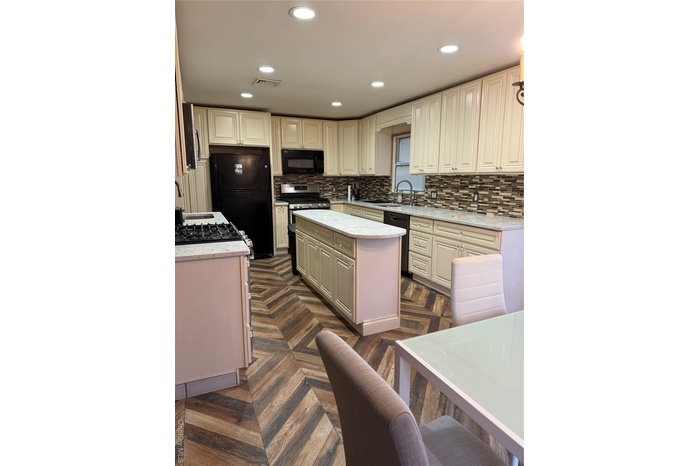 Kitchen featuring light stone counters, cream cabinets, a kitchen island, refrigerator, and dishwashing machine