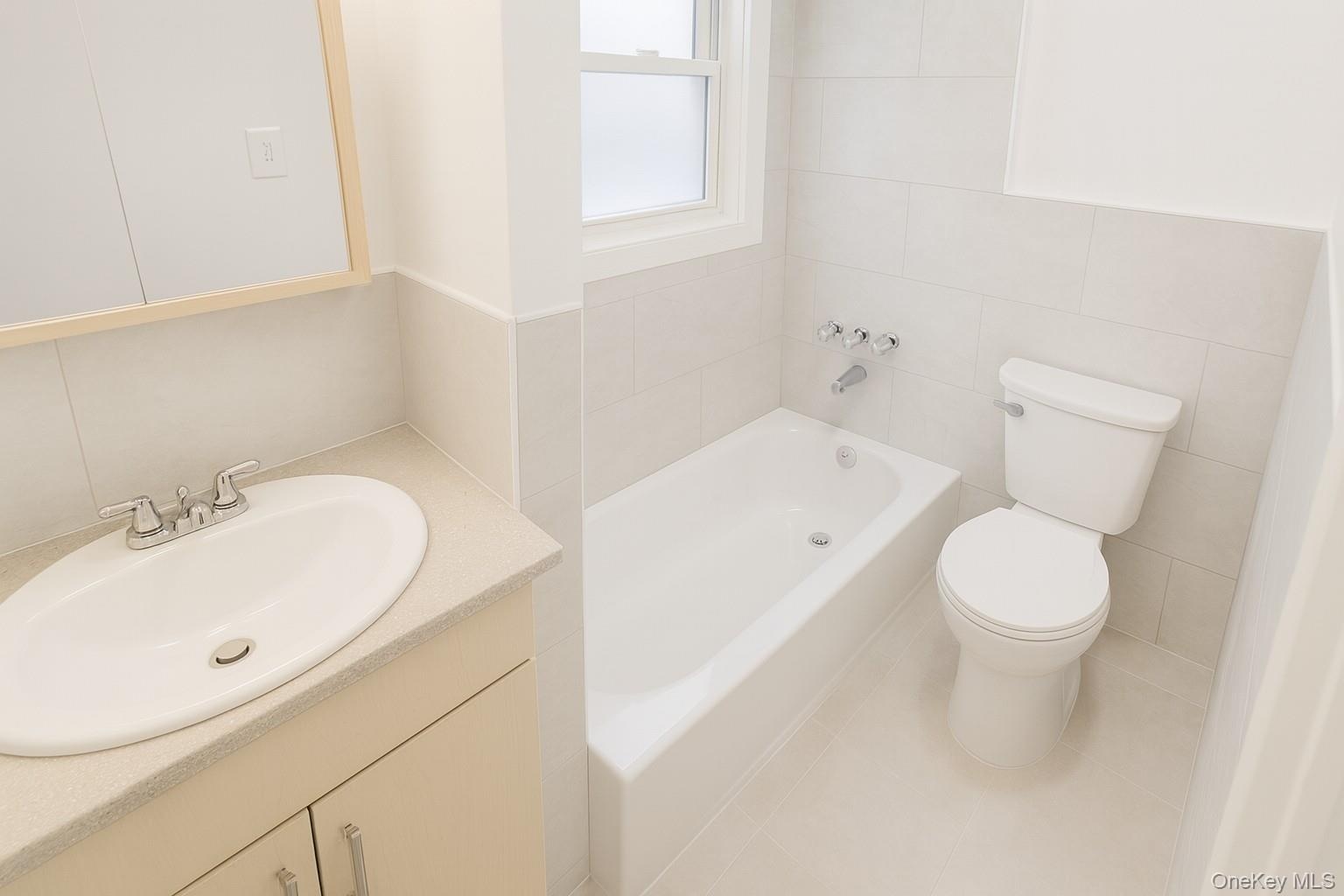 Full bathroom featuring a bath, vanity, tile walls, and tile patterned flooring